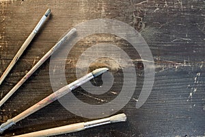Four paint brushes laying ontop of a wooden background
