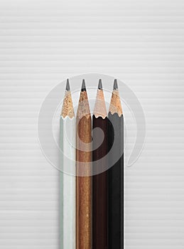 Four pencils, white brown dark brown and black, on white corrugated plastic board