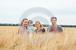 Four people family portrait, father, mother, teen age girl and toddler kid sitting together in yellow wheat stems, looking at