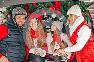 Four people, family with two children have Christmas party in car trunk, happy people spending time together, red