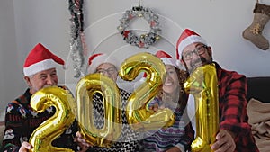 Four people having fun and smiling together at home holding up the four balloons numbers of the 2021 - family laughing and celebra
