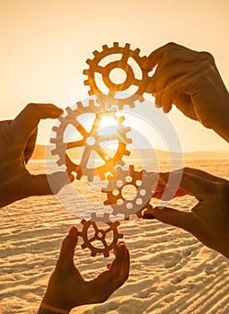 Four people hold gears on sunset background.