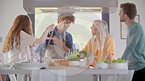 Four people talking while cooking together at home in modern kitchen.Young people cooking and preparing meal for lunch