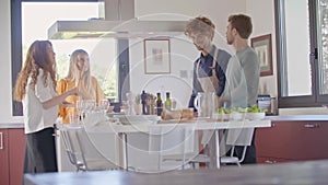 Four people talking while cooking together at home in modern kitchen.Young people cooking and preparing meal for lunch