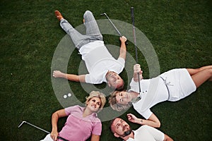 Four people, two guys and two girls, lie on the golf course and relax after the game
