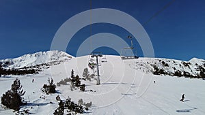 Four person ski chair lift going over mountain pistes in a ski resort with a blue sky