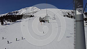 Four person ski chair lift going over mountain pistes in a ski resort with a blue sky