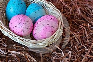 Four pink and blue Easter eggs in a basket on wooden floor covered with straw background