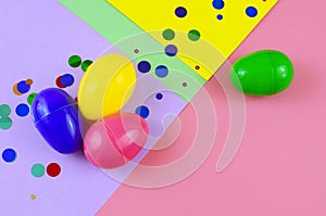 Four plastic easter eggs in blue, green, yellow and pink, with confetti on a geometric mutli-colored background