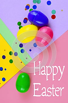 Four plastic easter eggs in blue, green, yellow and pink, with confetti on a geometric mutli-colored background