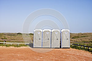 Four portable toilets in gravel parking lot