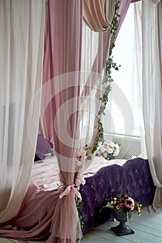 Four-poster bed in a bright interior in pink and purple tones.