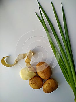 Four potatoes, one half peeled with freshly cut green onion. Vertical photo