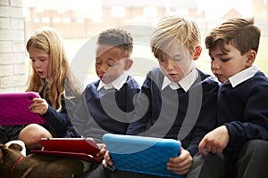 Four primary school children sitting on the floor in front of a window using tablet computers during break time, close up