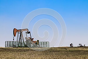 Four pumpjacks extracting oil or gas out on the horizon of a winter field under blue sky