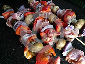 Four raw organic pork skewers on a clean black kitchen surface