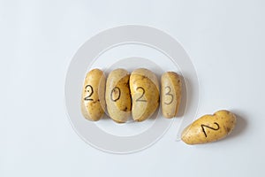 Four raw potatoes with the numbers 2023 and next to them lies a potato with the number 2, written in black felt-tip pen, lie on a