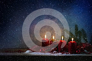 Four red advent candles burning in the snow on a rustic wooden b