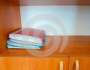 Four red and blue folders on a wooden shelf in the cabinet