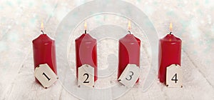 Four red burning advent candles on snowy white wooden background