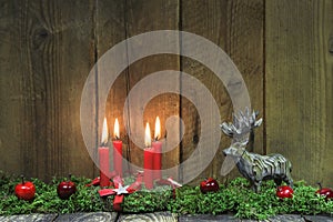 Four red burning christmas candles on wood background with deer.