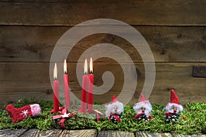 Four red burning christmas candles on wooden background with green moss.