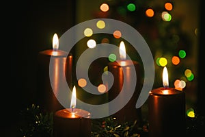 Four red candles burning on advent wreath with blurred colorful christmas tree with glowing lights in the background on evening