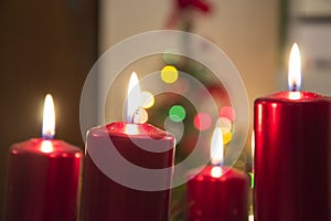 Four red candles burning on advent wreath with blurred colorful christmas tree with glowing lights in the background on evening