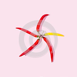 Four red and one yellow chili peppers arranged in a form of a star or a windmill. Pastel pink background. Happy healthy joyful