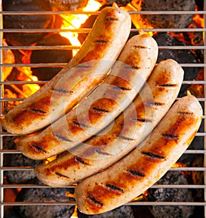 Four sausages called bratwurst, grilling over hot coals on a BBQ