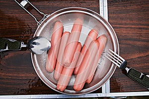 Four sausages frankfurter wurst boiling in hot water in pan.
