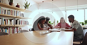 Four schoolmates talking sit at table in college library