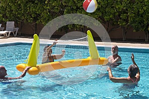 Four senior people friends or family in active elderly vacation having fun in swimming pool with balloon and volleyball - happy