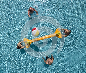 Four senior people in the swimming pool with inflatable net and ball. Two elderly brothers and their wifes having fun. Bright