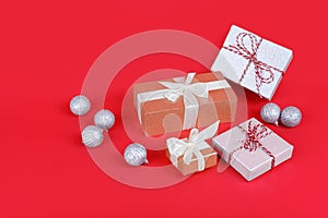 Four shimmering wrapped gift boxes with silver christmas balls on bright red background. New year celebration concept