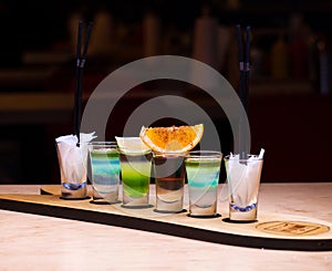 Four shots with alcoholic cocktails on a wooden plank