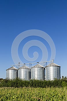 Four silver silos in field under blue sky