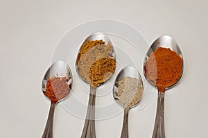 Four silver spoons with piles of spices on them on a white table. Middle Eastern and Asian grounded spices like cayenne pepper,