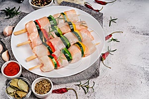 Four skewers with four pieces of chicken fillet with zucchini vegetables and bell peppers on a white plate on a light background