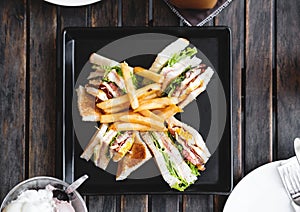 Four slices sandwiches with french fried, on black square dish, on wooden table
