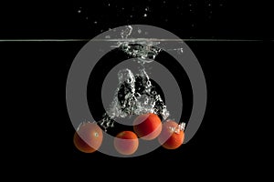 Four  small tomatoes falls under water with splash in a dark background