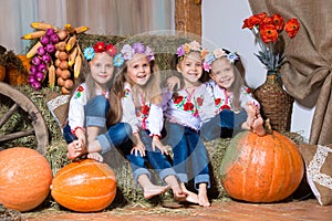 Four smiling girls twin sisters in Ukrainian wreaths sitting on haystacks. Autumn decor, harvest with pumpkins