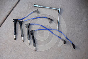 Four Spark Plugs and Blue Wires with Socket Wrench on Driveway