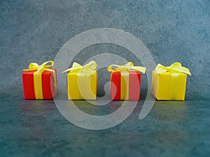 Four square red and yellow gift boxes on green textured background, Four neatly in a row.