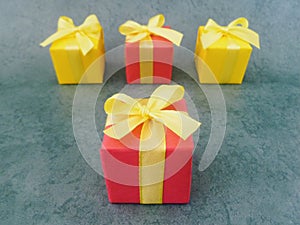 Four square red and yellow gift boxes on green textured background, Three in a row neatly at the back and one at the front .