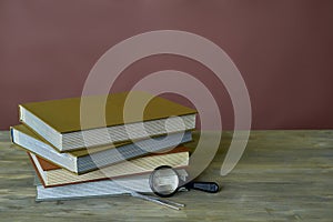 Four stamp albums books bunch, magnifier and tweezers on wooden table and bordeaux background