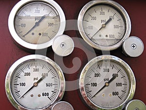 Four steel-rimmed pressure gauges on maroon-red background