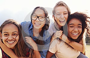 Four teenage girls having fun piggybacking outdoors