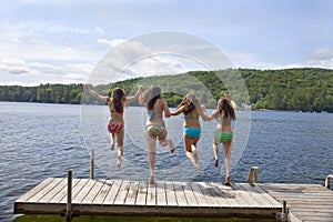 Four teenage girls jumping off dock at lake