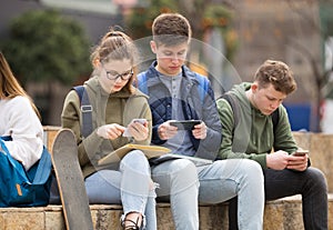 Four teenagers enthusiastically look at the screens of their smartphones on street